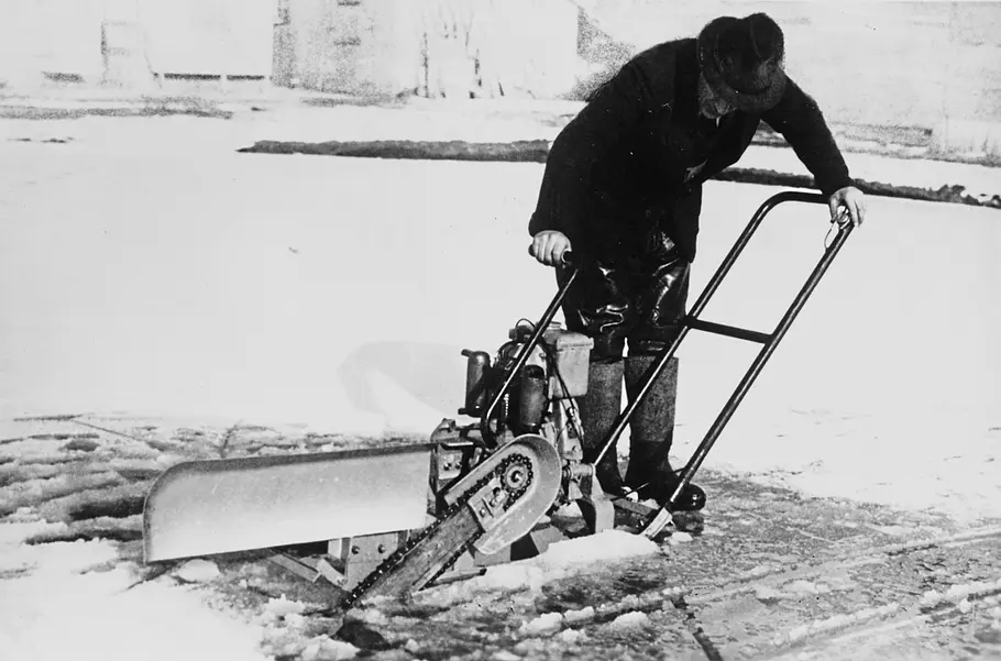 Historische Schwarz-Weiß-Aufnahme eines Mannes, der mit einer motorisierten Säge eine vereiste Fläche bearbeitet.