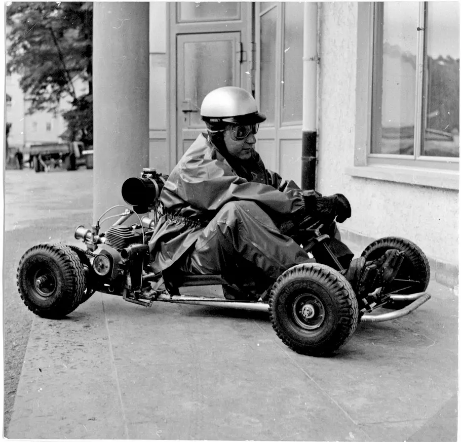 Historische Schwarz-Weiß-Aufnahme eines Mannes mit Helm und Schutzbrille in einem motorisierten Gokart.