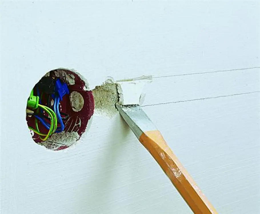 Unterputzdose setzen Mit einem Meißel wird Putz um eine geöffnete Wanddose für die Installation freigelegt.