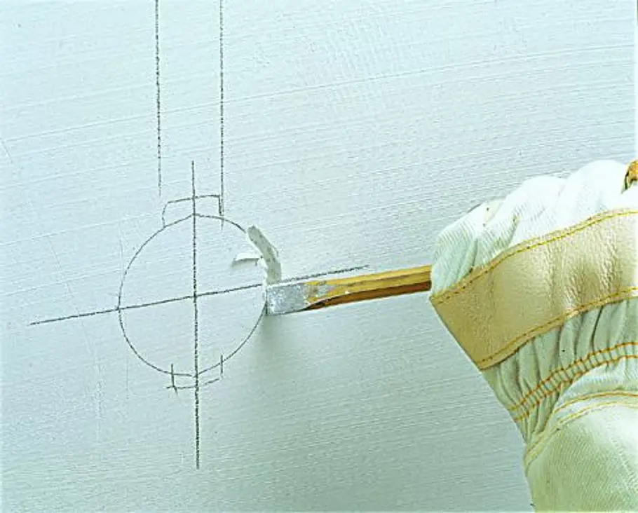Unterputzdose setzen Ein Handschuh hält einen Meißel an eine angezeichnete Kreisform auf der Wand zum Vorbereiten einer Dose.
