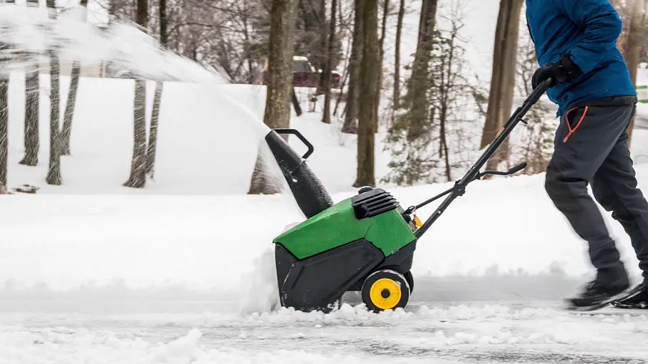 motorisiertes Schneeräumgerät: Schneefräse Ein Mann schiebt eine Schneefräse durch den Schnee, der im hohen Bogen zur Seite geblasen wird.