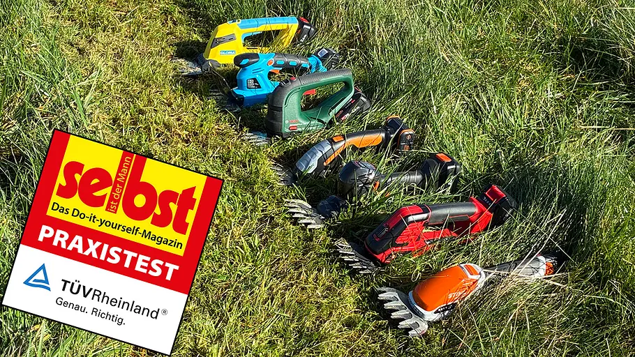Grasscheren im Test Mehrere akkubetriebene Grasscheren in verschiedenen Farben liegen nebeneinander auf einer Wiese mit hohem Gras.