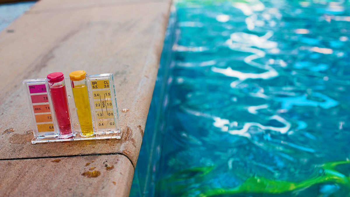 Pooltest-Set zur Messung von pH- und Chlorgehalt steht am Beckenrand vor klarem Wasser – wichtig zur Vorbeugung von Algenbildung.