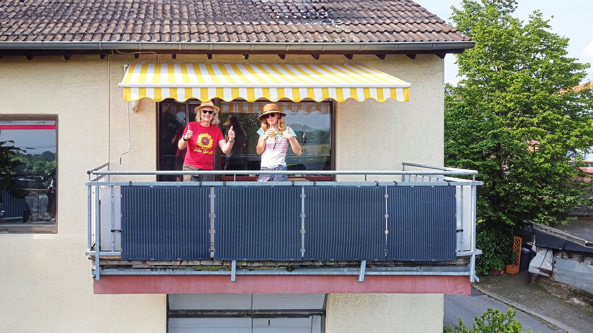 Zwei Personen auf Balkon, am Geländer ein Balkonkraftwerk