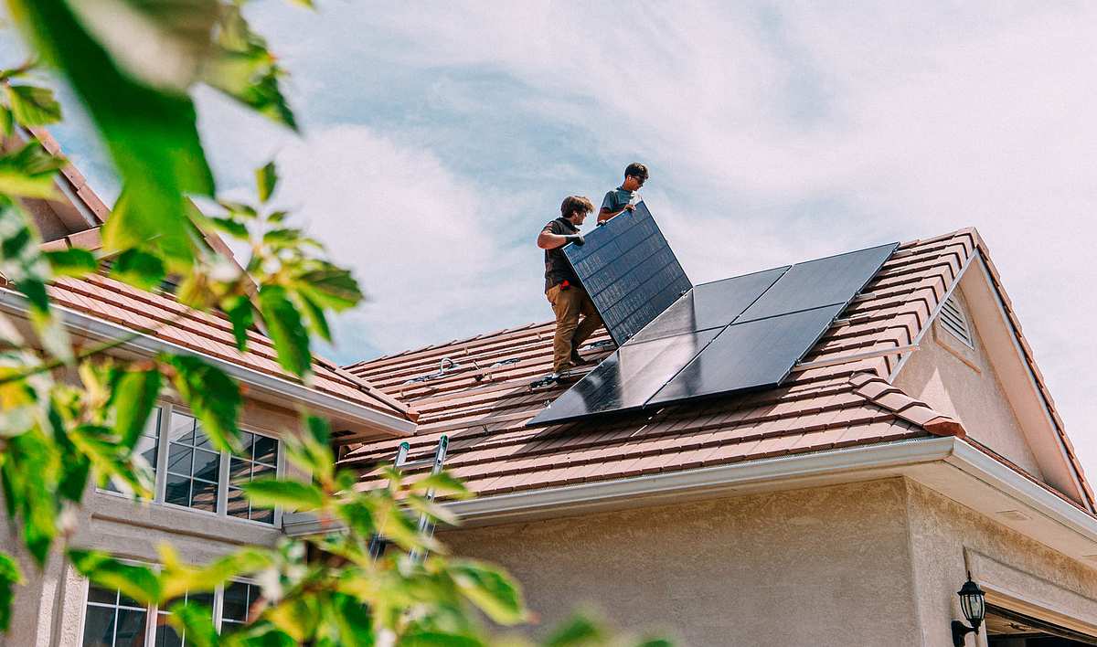Installation PV-Anlage Zwei Personen bringen große Solarmodule auf einem Hausdach an
