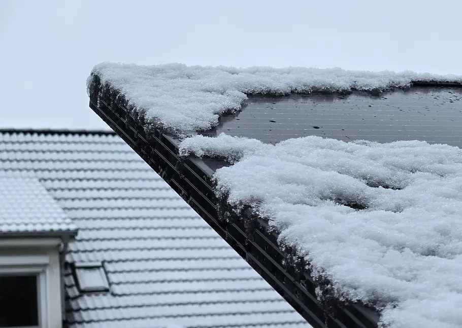 Balkonkraftwerk-Schnee-Dach Schnee liegt auf einem Solarpanel, im Hintergrund ist ein Hausdach mit Schnee zu sehen