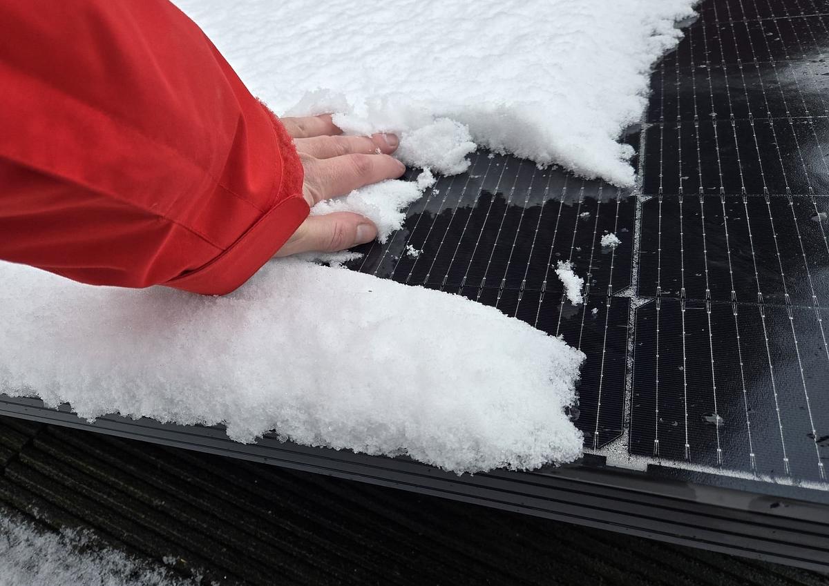 Solarmodul mit Schnee Mit einer Hand wird Schnee von einem Solarmodul abgewischt.