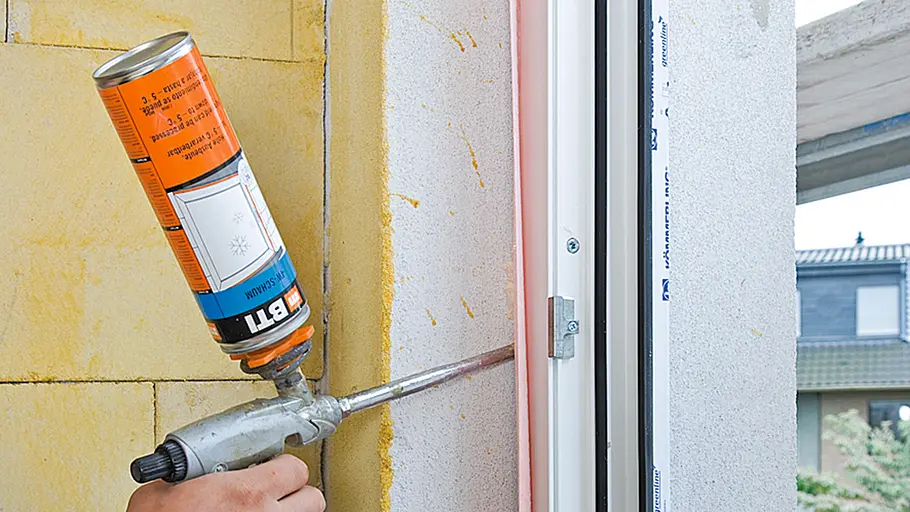 Schaumpistole Eine Hand bringt mit einer Schaumpistole Bauschaum in den Spalt zwischen Fensterrahmen und Wand ein.
