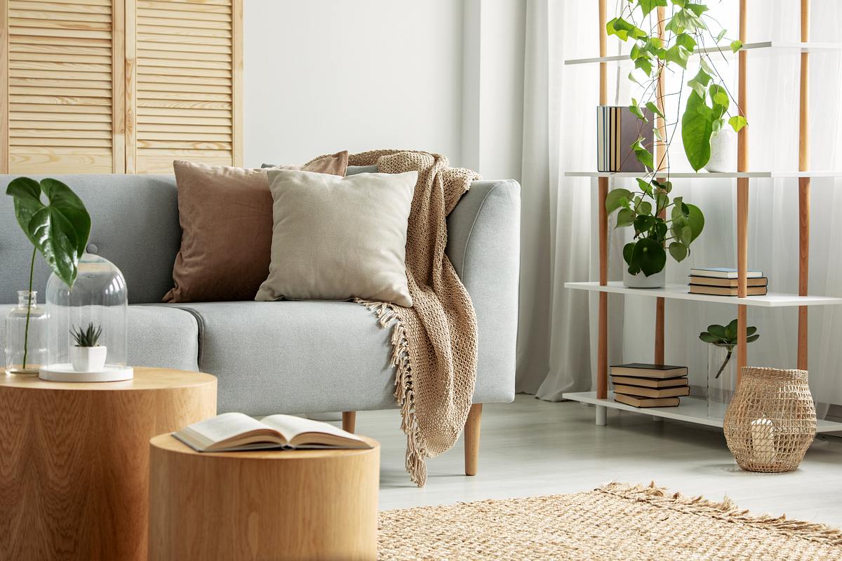 Ein modernes Wohnzimmer mit einem grauen Sofa, Pflanzen und kuscheligen Decken