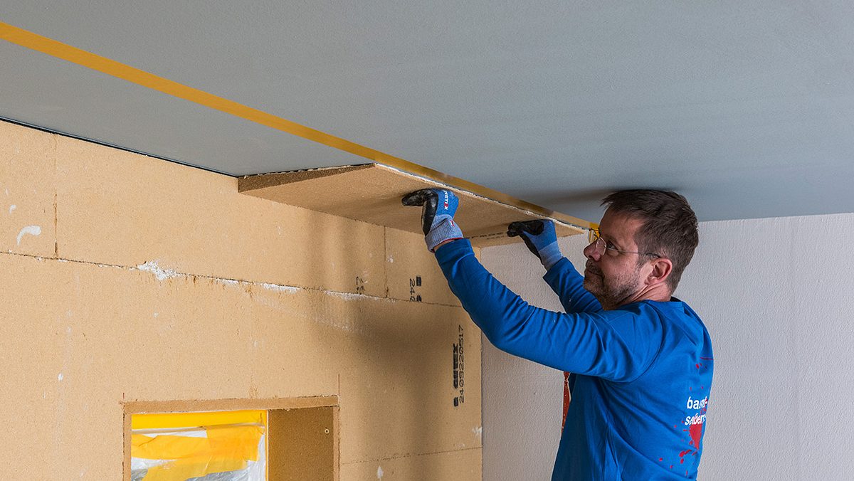 Ein Mann mit blauer Kleidung befestigt eine Dämmplatte an einer Decke.