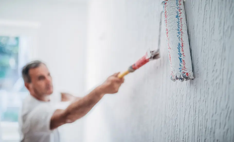 Mann streicht eine Wand mit einem Farbroller