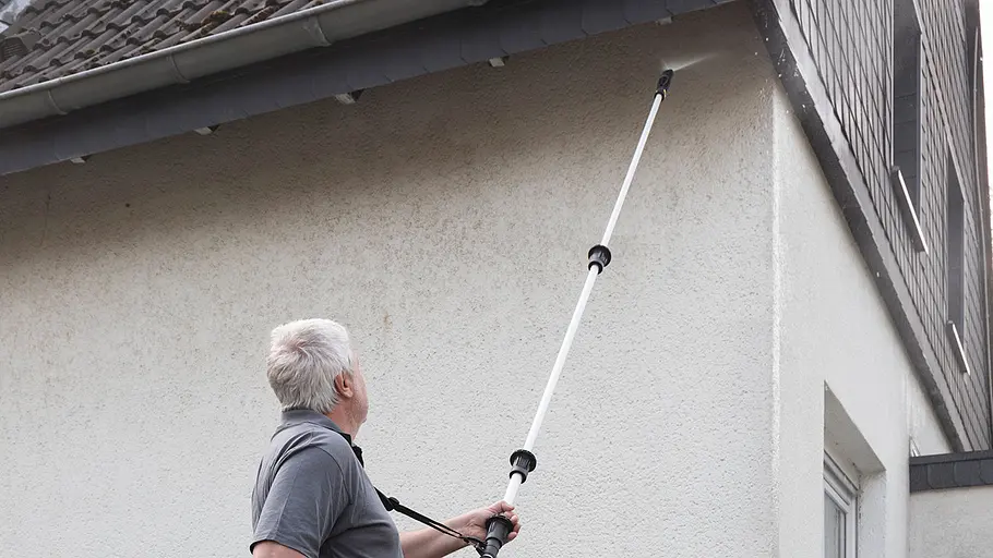 Fassade streichen Ein Mann mit grauen Haaren reinigt die Außenfassade eines Hauses mit einem Hochdruckreiniger an einer Teleskopstange.