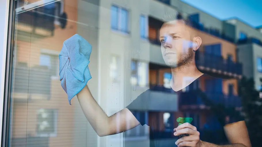 Ein junger Mann steht hinter einer streifenfrei geputzten Glasscheibe und poliert letzte Schlieren aus dem Glas