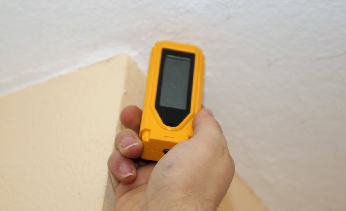 Eine Hand mit einem Feuchtigkeitsmessgerät an der Wand.