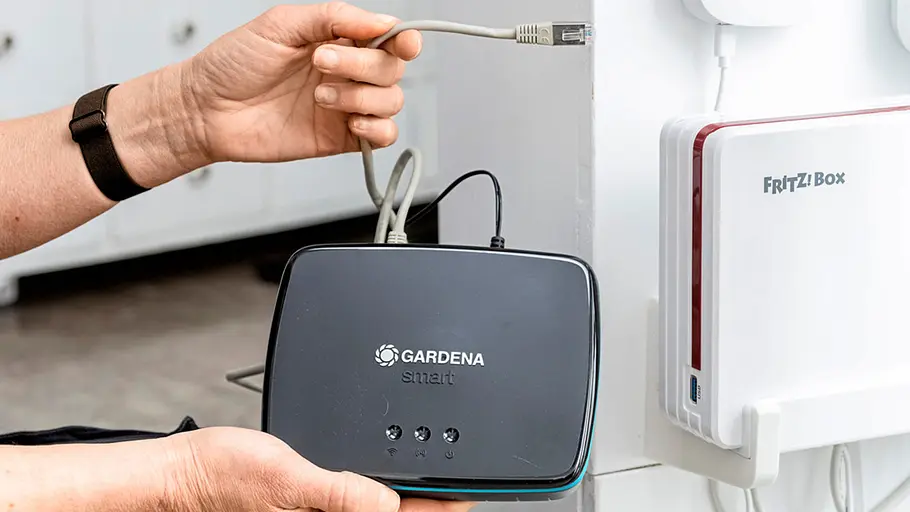 Gardena Smart Water Control Eine Person hält eine Gardena Smart Water Control-Basisstation und steckt ein Netzwerkkabel in das Gerät ein.