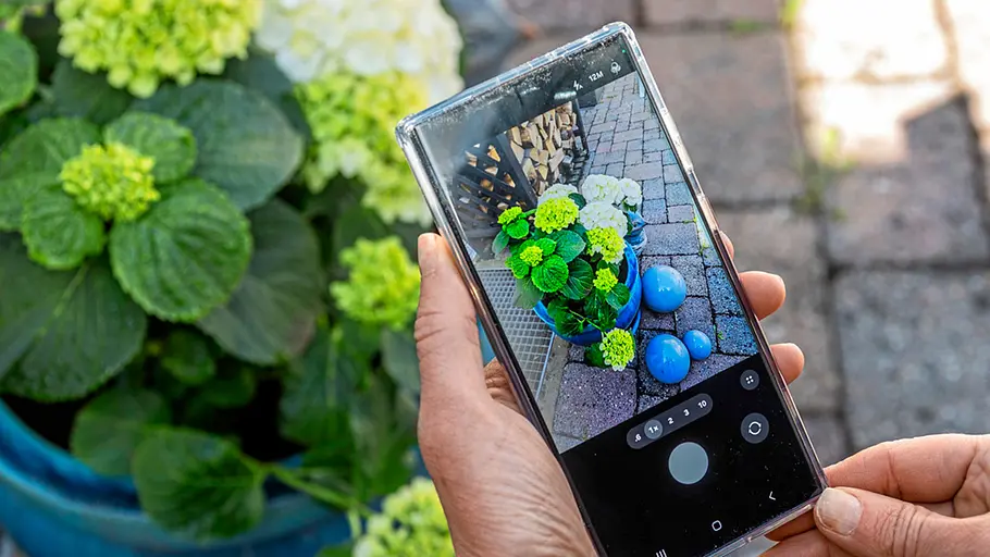 Gardena Smart Water Control Eine Person fotografiert mit dem Smartphone einen blühenden Hortensientopf und blaue Deko-Kugeln auf der Terrasse.