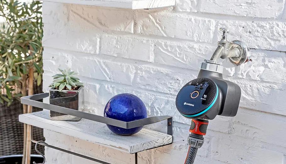 Gardena Smart Water Control Ein Gardena Smart Water Control ist an einem Wasserhahn einer weißen Backsteinwand angeschlossen.