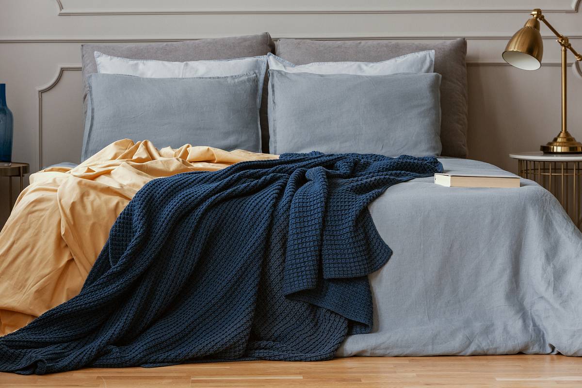 Ein graues Bett mit einer gelben und blauen Decke