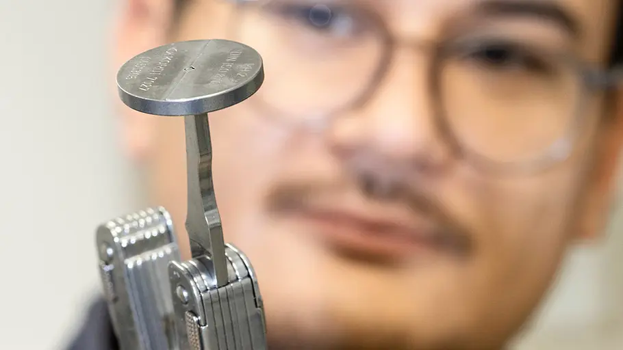 Multitool-Test Ein Mann mit Brille hält ein Multitool, an dessen Spitze eine runde Metallplatte befestigt ist, in der Hand.