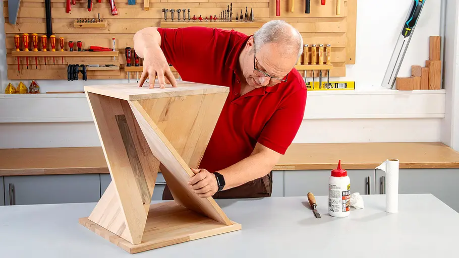 Verdrehter Hocker Ein Mann setzt in einer Werkstatt die abgeschrägten Platten eines verdrehten Hockers passgenau zusammen.
