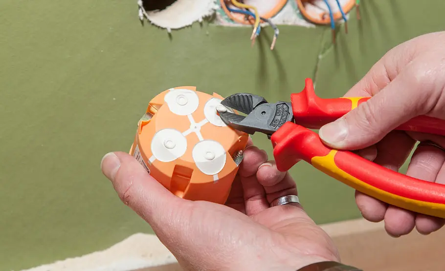 Steckdose anschließen Mit einer Zange werden Öffnungen an einer orangefarbenen Hohlwanddose herausgetrennt.
