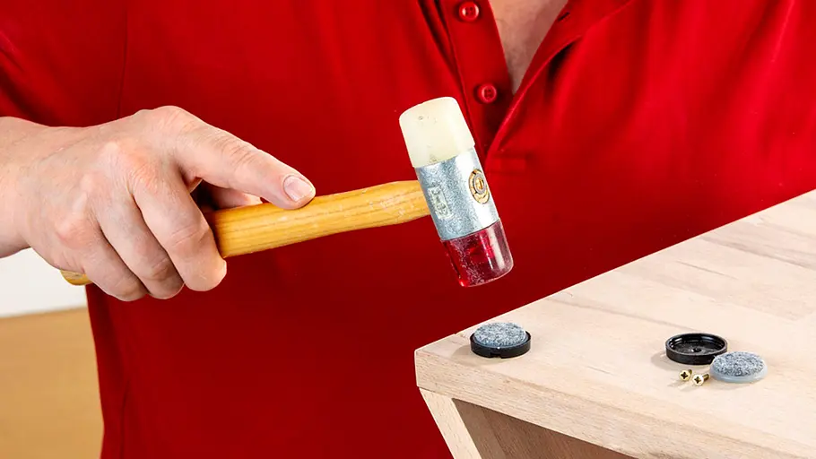 Verdrehter Hocker Mit einem Gummihammer wird ein Filzgleiter an die Unterseite einer Holzkante vom verdrehten Hocker befestigt.