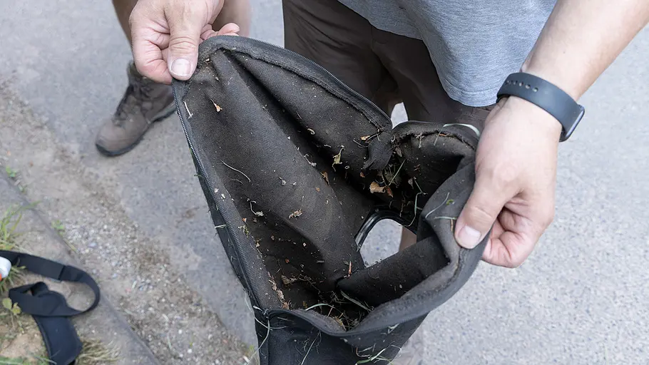 Eine Person hält einen geöffneten Fangsack mit Gras- und Laubresten weit geöffnet in den Händen.