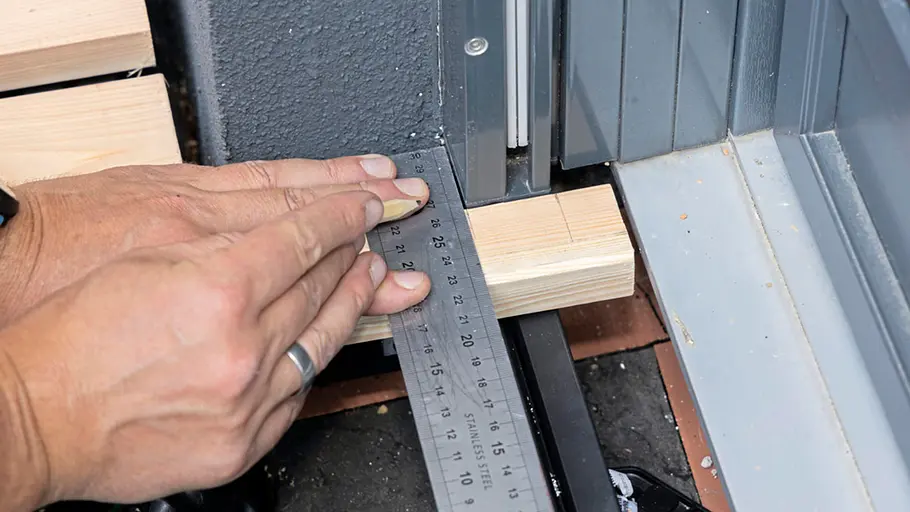 Terrasse gestalten Mit einem Metallwinkel und einem Bleistift wird eine Holzleiste passgenau vor einer Terrassentür markiert.