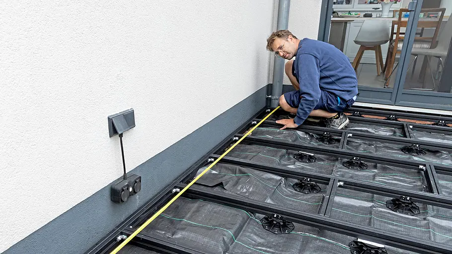 Terrasse gestalten Ein Mann misst mit einem Maßband die Länge der Terrasse aus, auf der ein Unterbau für den Terrassenboden verlegt wird.