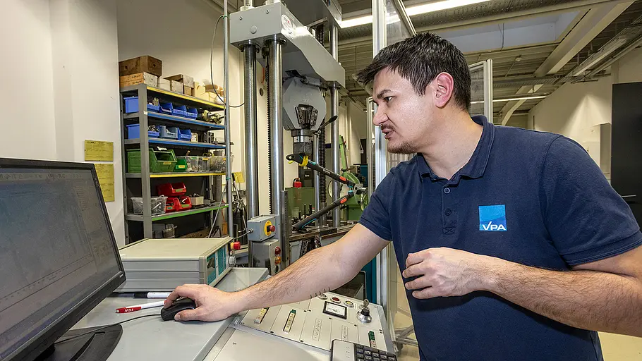 Astscheren-Test Prüflast Ein Mann steuert an einem Computer eine Prüfmaschine im Labor, im Hintergrund stehen Werkzeuge und eine Astschere in der Vorrichtung.