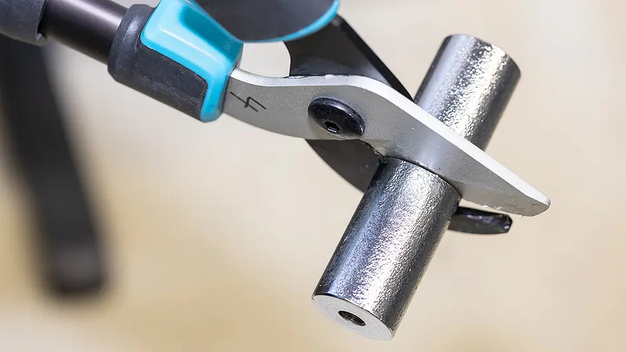 Astscheren-Test Belastungstest Eine Astschere mit blauem Griff testet ihre Schneidkraft an einem runden Metallstab unter Laborbedingungen.