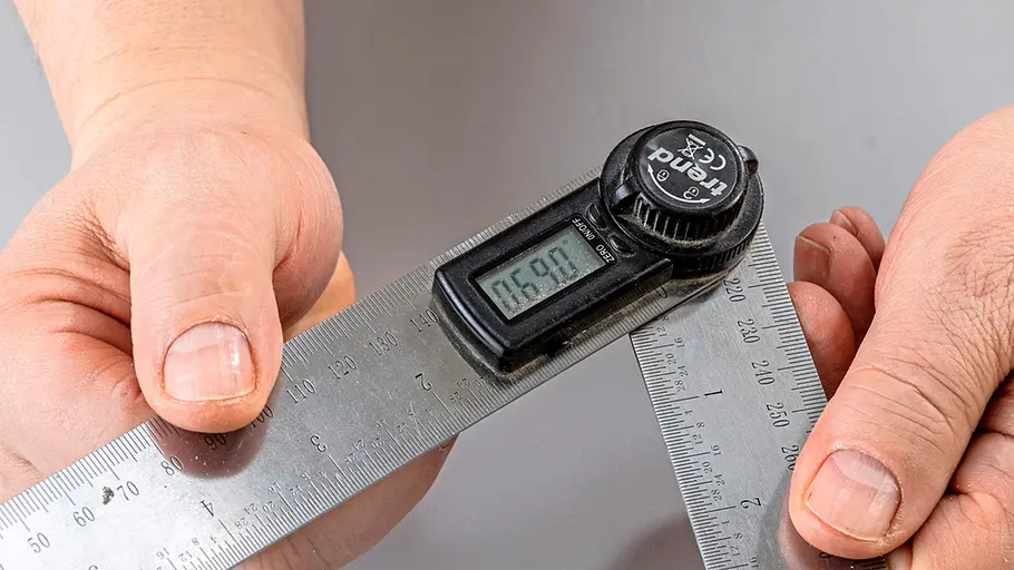Verdrehter Hocker Zwei Hände halten einen digitalen Winkelmesser, der zwei Metallwinkel mit einer Anzeige von 60 Grad misst.
