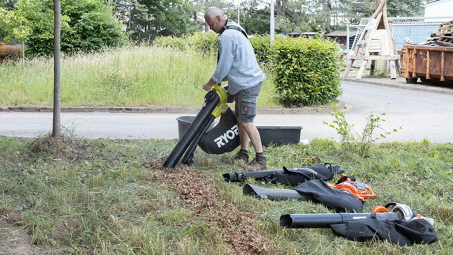 Ein Mann arbeitet mit einem gelben Laubsauger auf einer Wiese, mehrere Laubsauger liegen im Gras vor ihm.