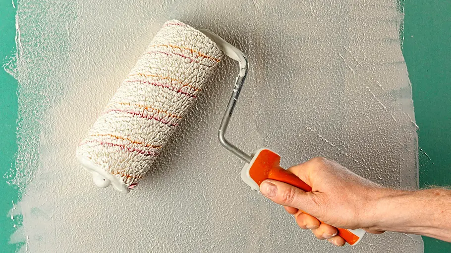Spachtelmasse Mit einer Farbrolle wird weiße Spachtelmasse gleichmäßig auf eine grüne Wand aufgetragen.