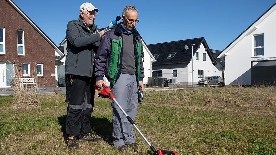 Akku-Grasscheren-Test: Lautstärke Zwei Männer stehen auf einer Wiese, einer misst mit einem Schallpegelmessgerät die Lautstärke einer Akku-Grasschere am Ohr des anderen.