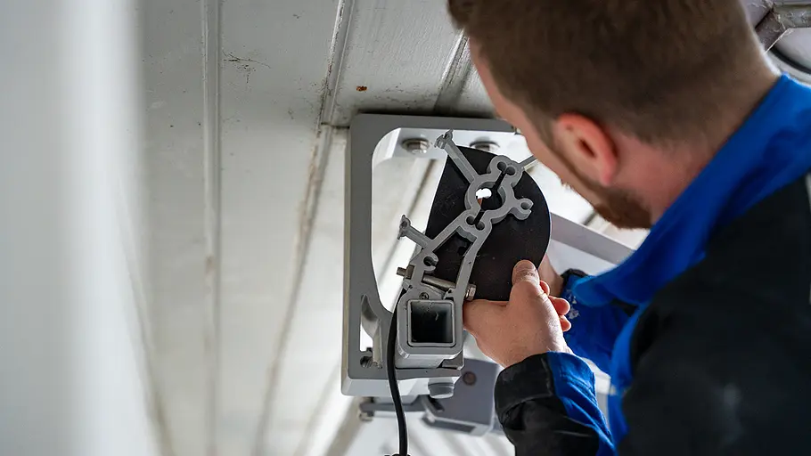 Motorlager befestigen Ein Mann fixiert das Motorlager der Markise mit einer Metallhalterung an der Decke einer überdachten Terrasse.
