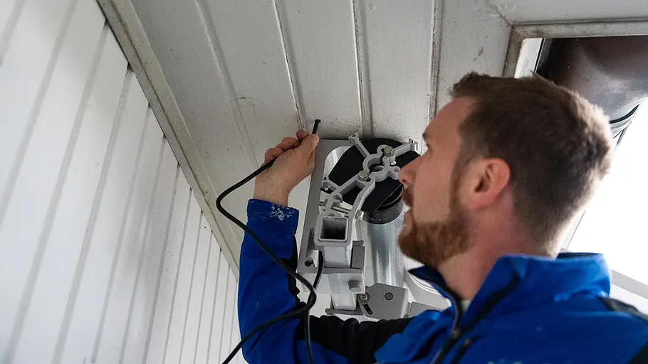 Leitung nach innen führen Ein Mann führt das Stromkabel des Markisenmotors durch ein Loch in der Holzdecke in den Innenraum.