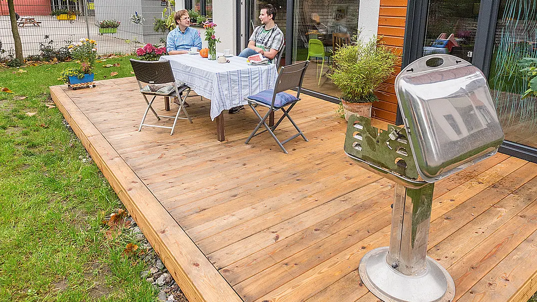 Zwei Männer am Gartentisch auf der Veranda, im Vordergrund ein Grill - Foto: sidm / CK