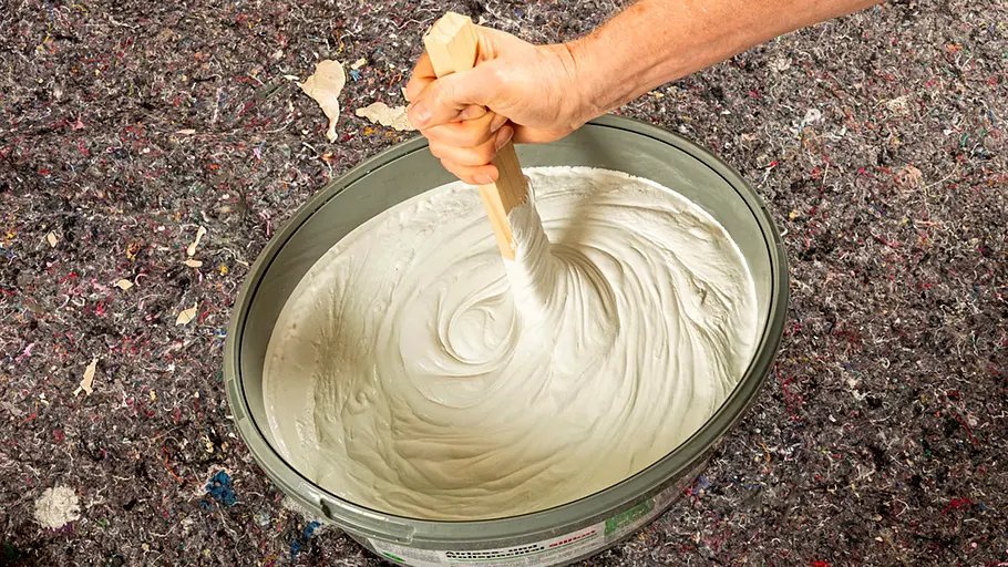 Spachtelmasse Ein Eimer mit weißer, cremiger Spachtelmasse wird mit einem Holzstab kräftig umgerührt.