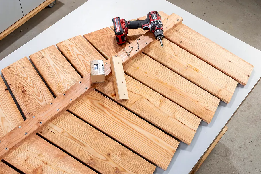 Gartendusche bauen Zwei blattförmige Holzelemente liegen mit Akkuschraubern und Verbindungshölzern auf einer Arbeitsfläche.