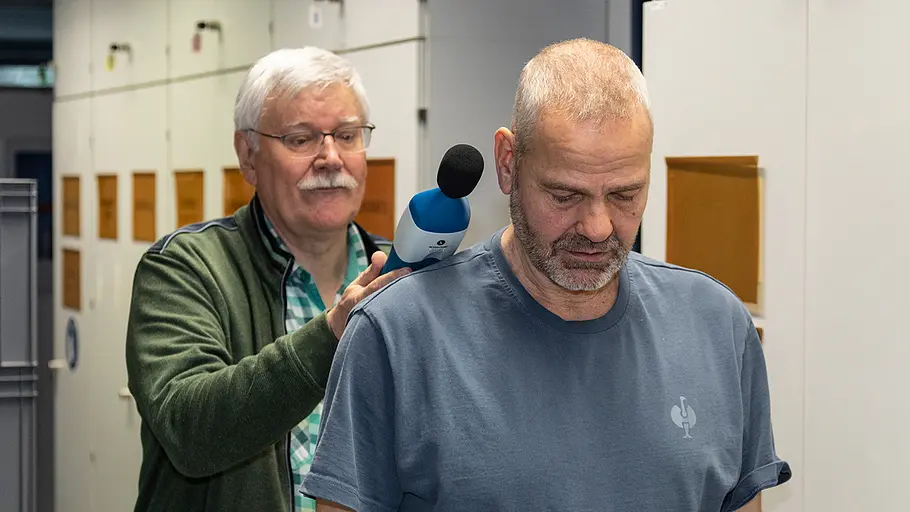 Lautstärke-Prüfung Ein älterer Mann misst mit einem Schallpegelmessgerät hinter einem zweiten Mann den Geräuschpegel in einem Technikraum.