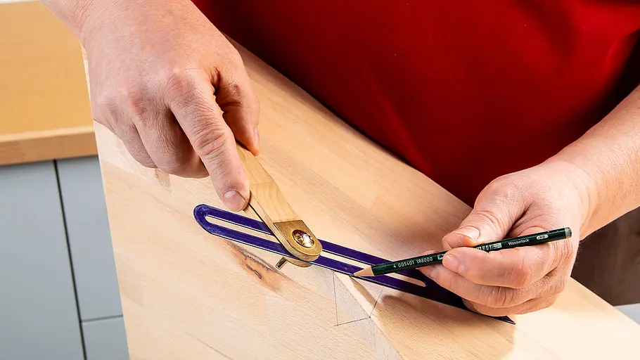 Verdrehter Hocker Eine Person zeichnet mit einem Schreinerwinkel und Bleistift eine schräge Linie auf ein helles Holzbrett in heller Umgebung.