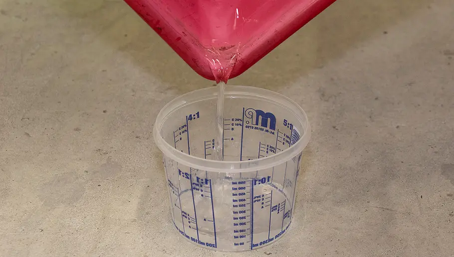 Nasssauger-Test Wasser wird aus einer roten Schale in einen transparenten Messbecher mit blauer Skala auf einem Betonboden gegossen.