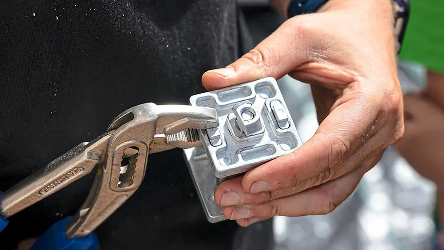 Terrasse gestalten Eine Person zieht mit einer Wasserpumpenzange die Schraube eines Metallverbinders für die Terrassen-Unterkonstruktion fest.