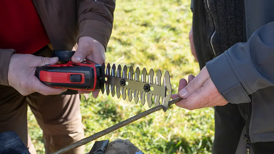 Akku-Grasscheren-Test: Schnittleistung Zwei Personen testen mit einer rot-schwarzen Akku-Schere an einem Holzrute die Schnittleistung des Geräts.