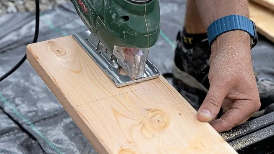 Terrasse gestalten Eine Person schneidet ein markiertes Holzbrett mit einer Stichsäge passend für die Terrasse zu.