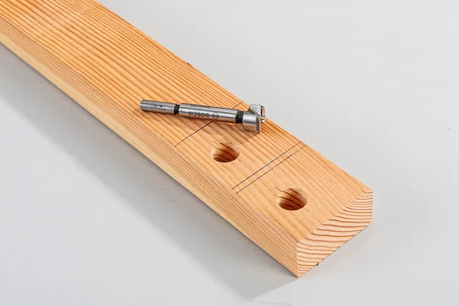 Gartendusche bauen Ein Holzbrett mit zwei gebohrten Löchern, angezeichneten Schnittlinien und einem Bohrer auf der Oberfläche.