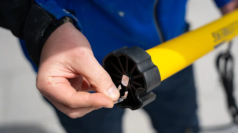 Kupplungsadapter Splint Eine Hand setzt einen Metall-Splint in die Öffnung eines schwarzen Kupplungsadapters am gelben Markisenmotor ein.