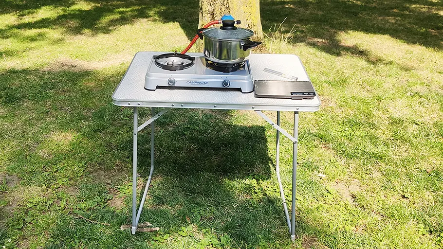 Campingaz Camping Cook CV Ein silberner Campingkocher mit zwei Kochplatten steht auf einem Tisch, darauf ein Topf und daneben eine digitale Waage.