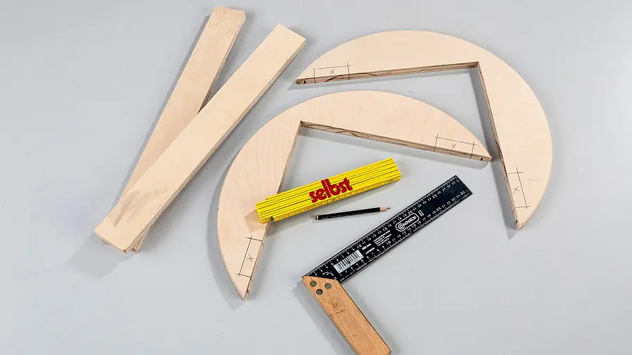 Aussparungen anzeichnen Zwei Holz-Viertelkreisrahmen und drei Holzbretter liegen mit Zollstock, Winkel und Bleistift auf grauem Untergrund bereit.
